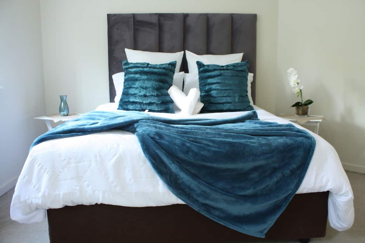 Un lit bien fait, avec une tête de lit sombre, une literie blanche et des coussins turquoise.