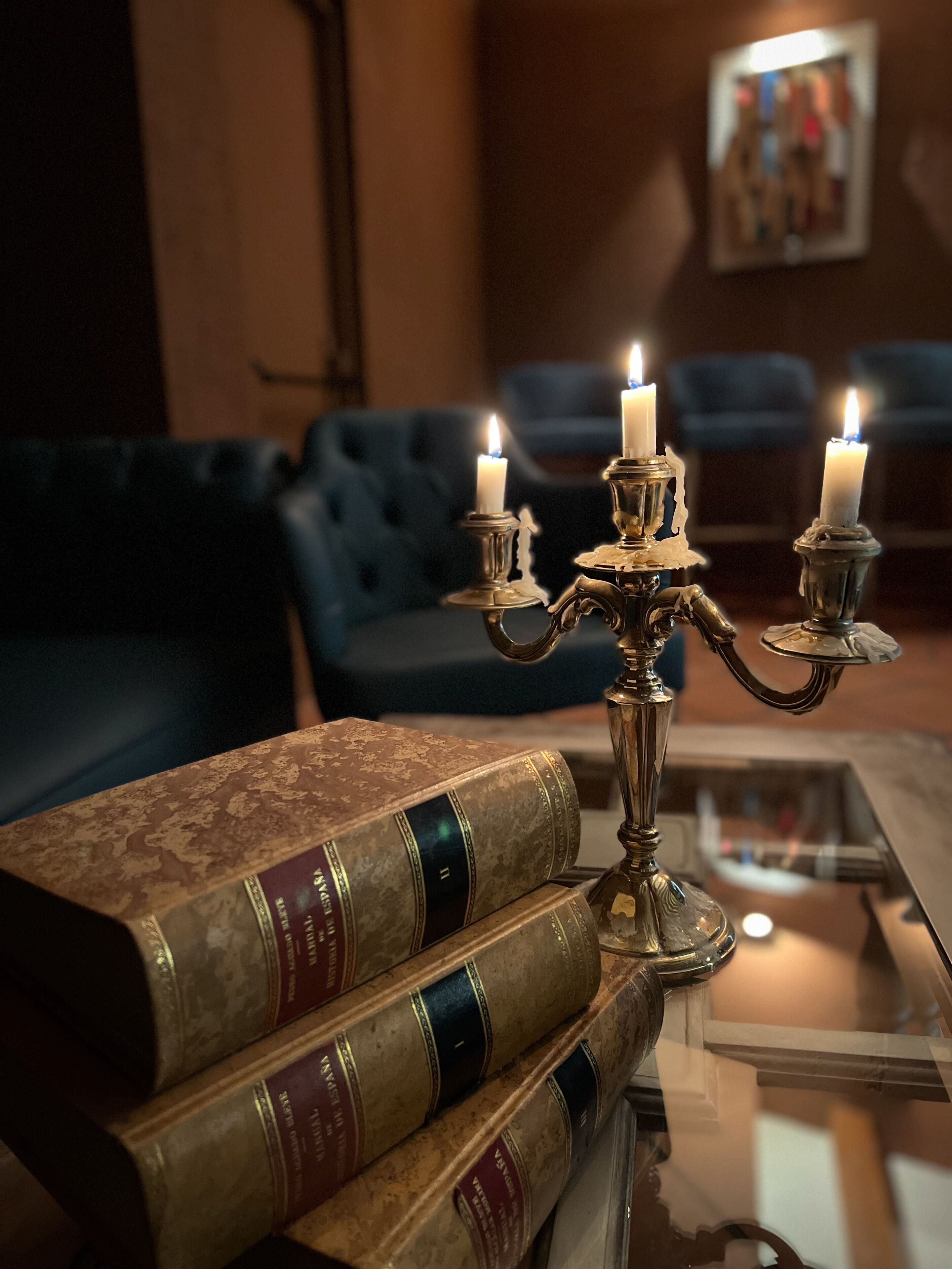 A room with a blue sofa, a brass candelabra with lit candles, and a stack of books on a glass table.