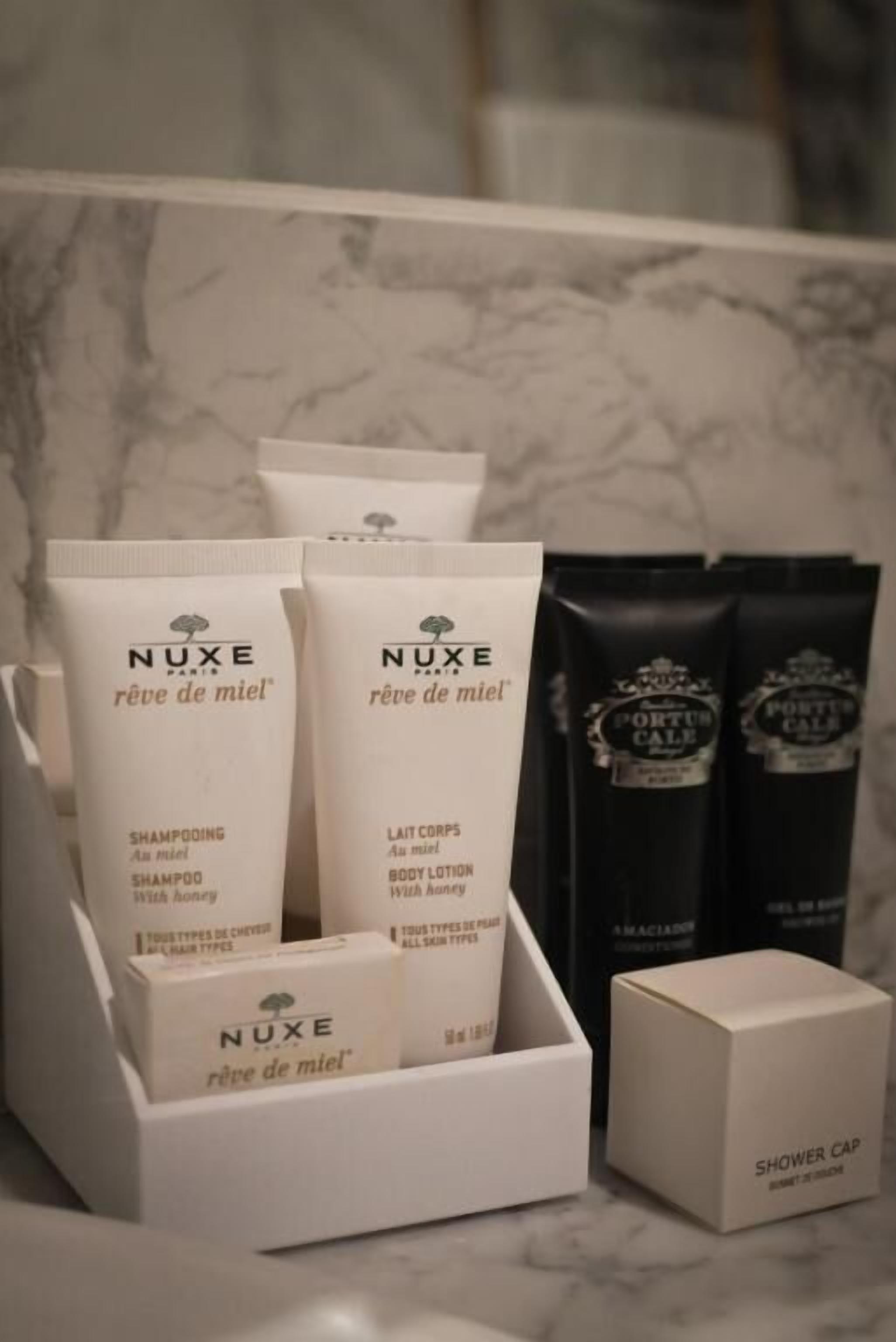 Un conjunto de productos de ducha Nuxe Paris que incluye champú, loción corporal y gorro de ducha sobre una encimera de mármol.