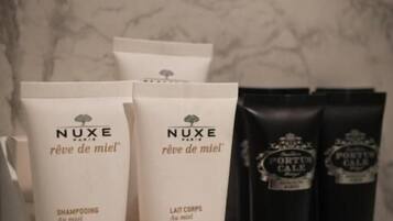 Un conjunto de productos de ducha Nuxe Paris que incluye champú, loción corporal y gorro de ducha sobre una encimera de mármol.