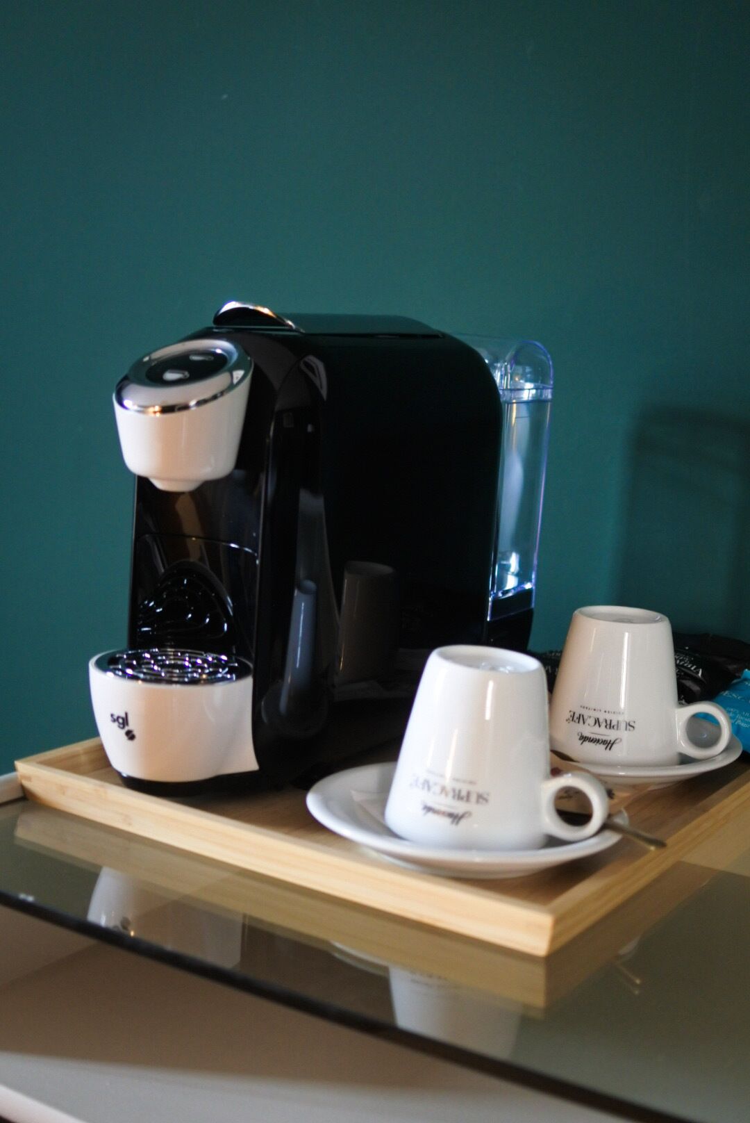 A coffee maker, two white cups, and a saucer on a wooden tray.