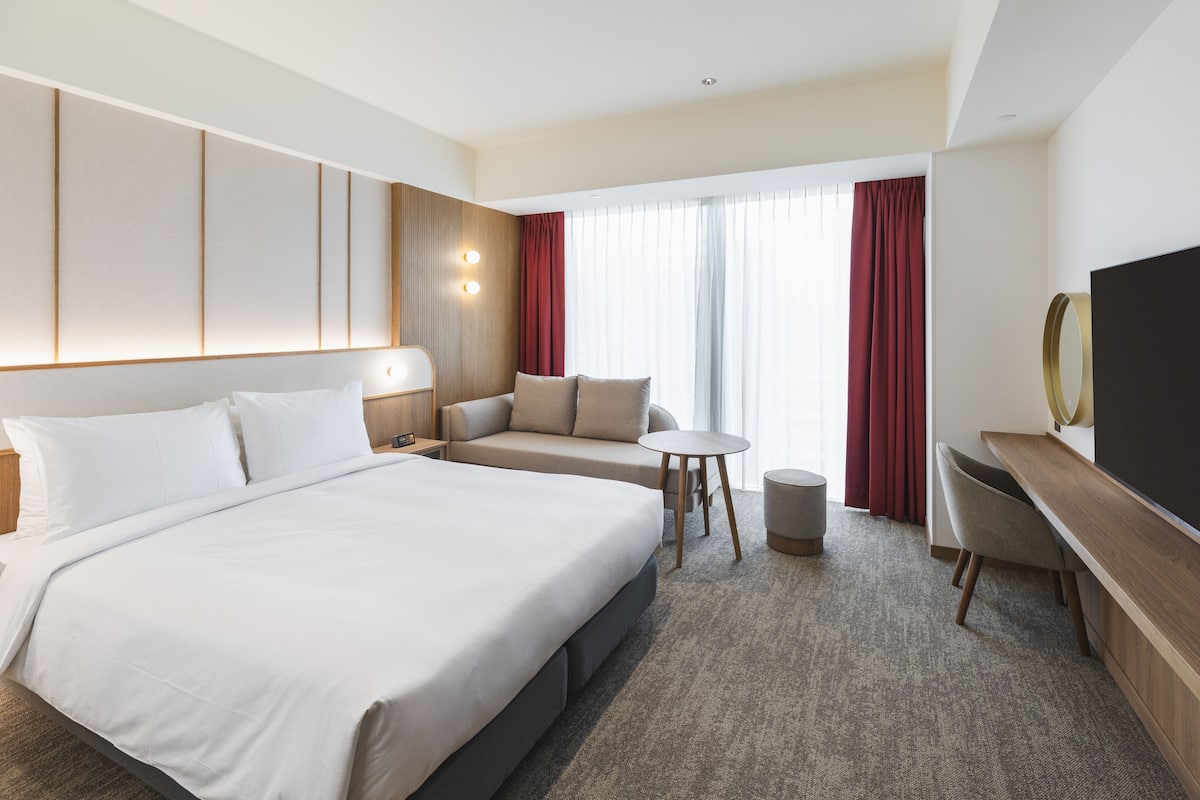 A hotel room with a large bed, a sofa, a small round table, a TV, and a desk.