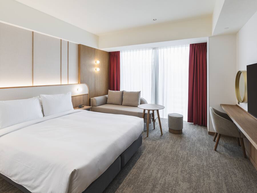A hotel room with a large bed, a sofa, a small round table, a TV, and a desk.