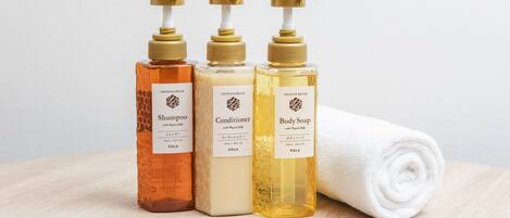 Tres botellas de productos de baño y una toalla enrollada sobre una superficie de madera.