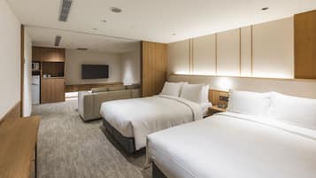 A hotel room with two beds, a sofa, a desk, a TV, and a kitchenette.