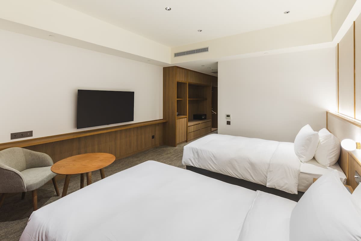 A hotel room with two beds, a TV, a wooden wardrobe, and a small round table.