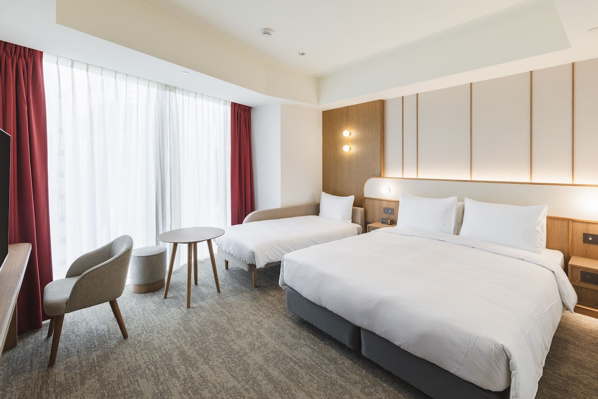 A hotel room with two beds, a desk, a chair, and a small table.