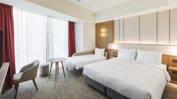 A hotel room with two beds, a desk, a chair, and a small table.