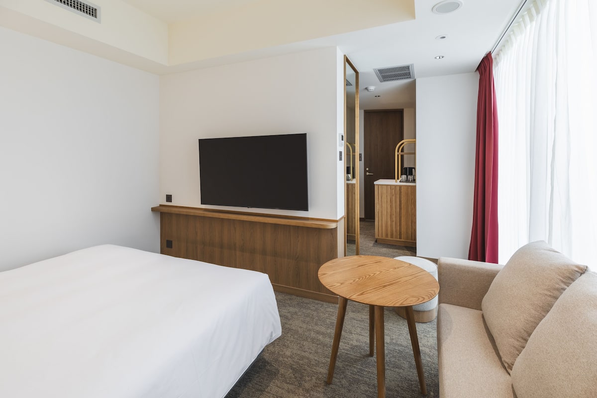 A hotel room with a bed, a small round table, a sofa, a TV, and a wooden cabinet.