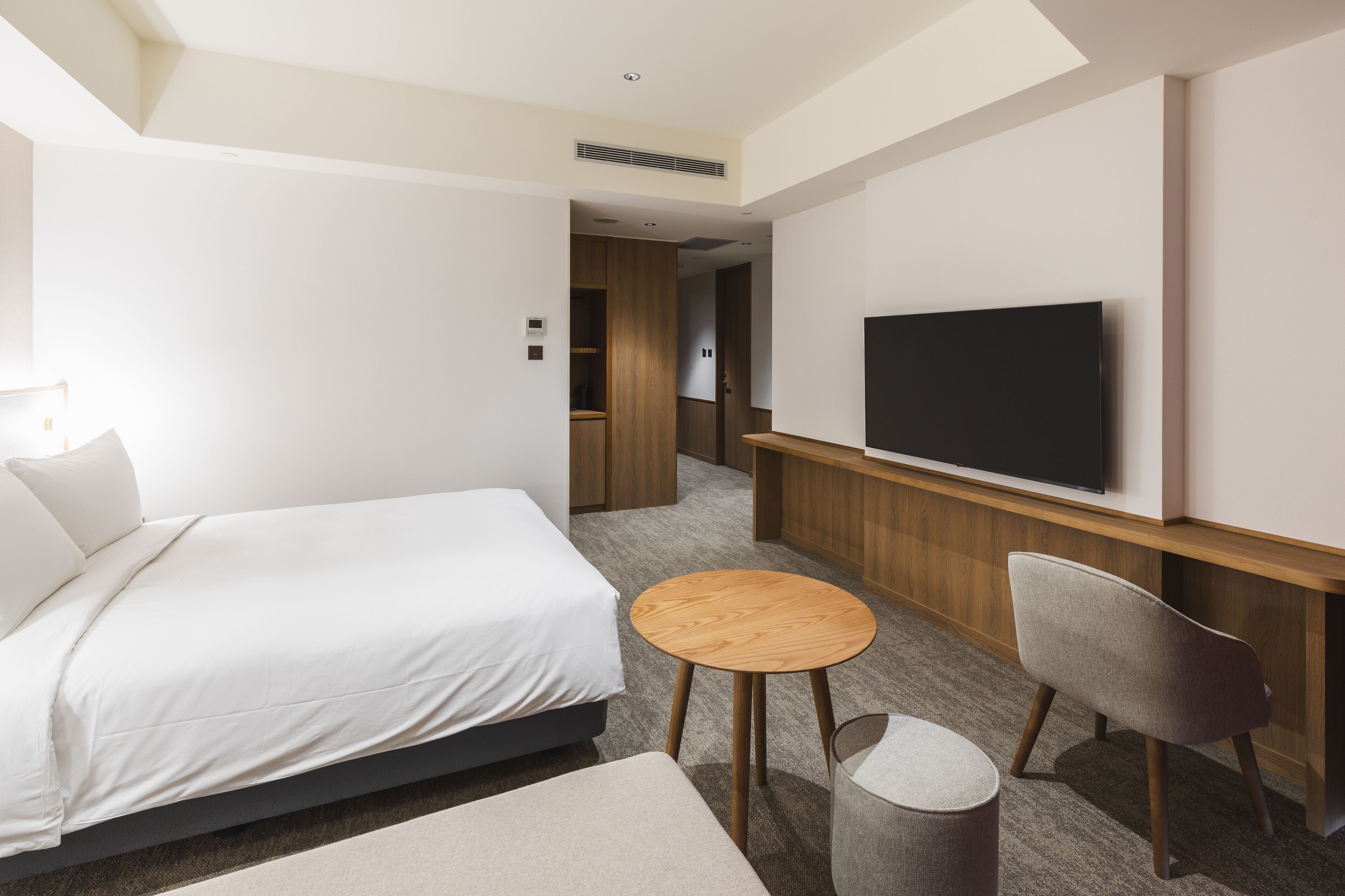 Een moderne hotelkamer met een bed, een aan de muur bevestigde televisie, een klein rond tafeltje en een stoel.