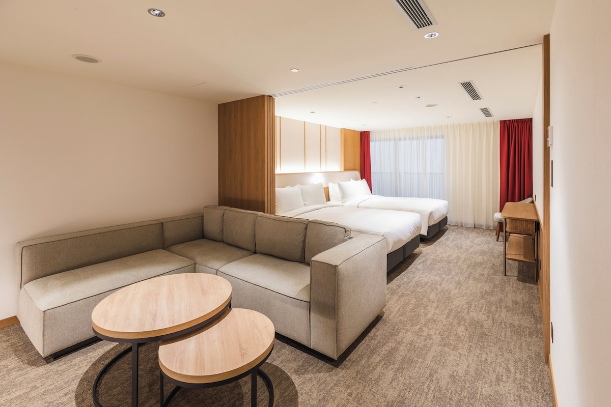 A hotel room with a sofa, two round tables, a bed, and a desk.