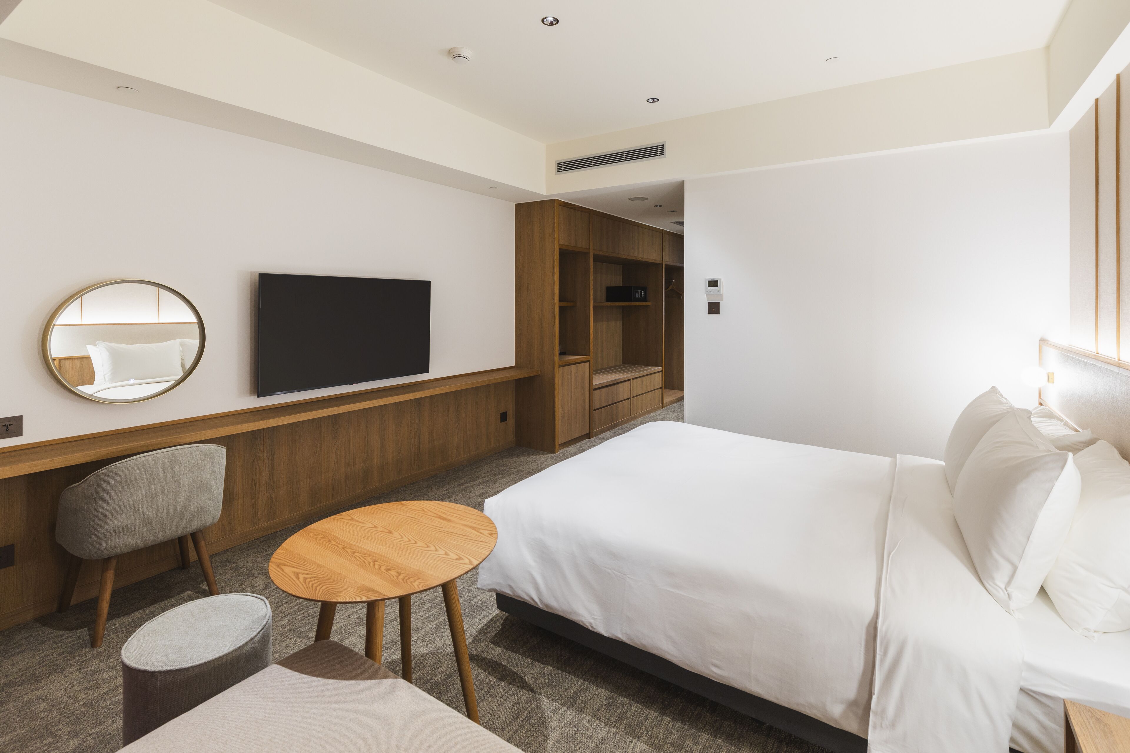 A modern hotel room with a large bed, a TV mounted on the wall, a wooden wardrobe, and a small round table.
