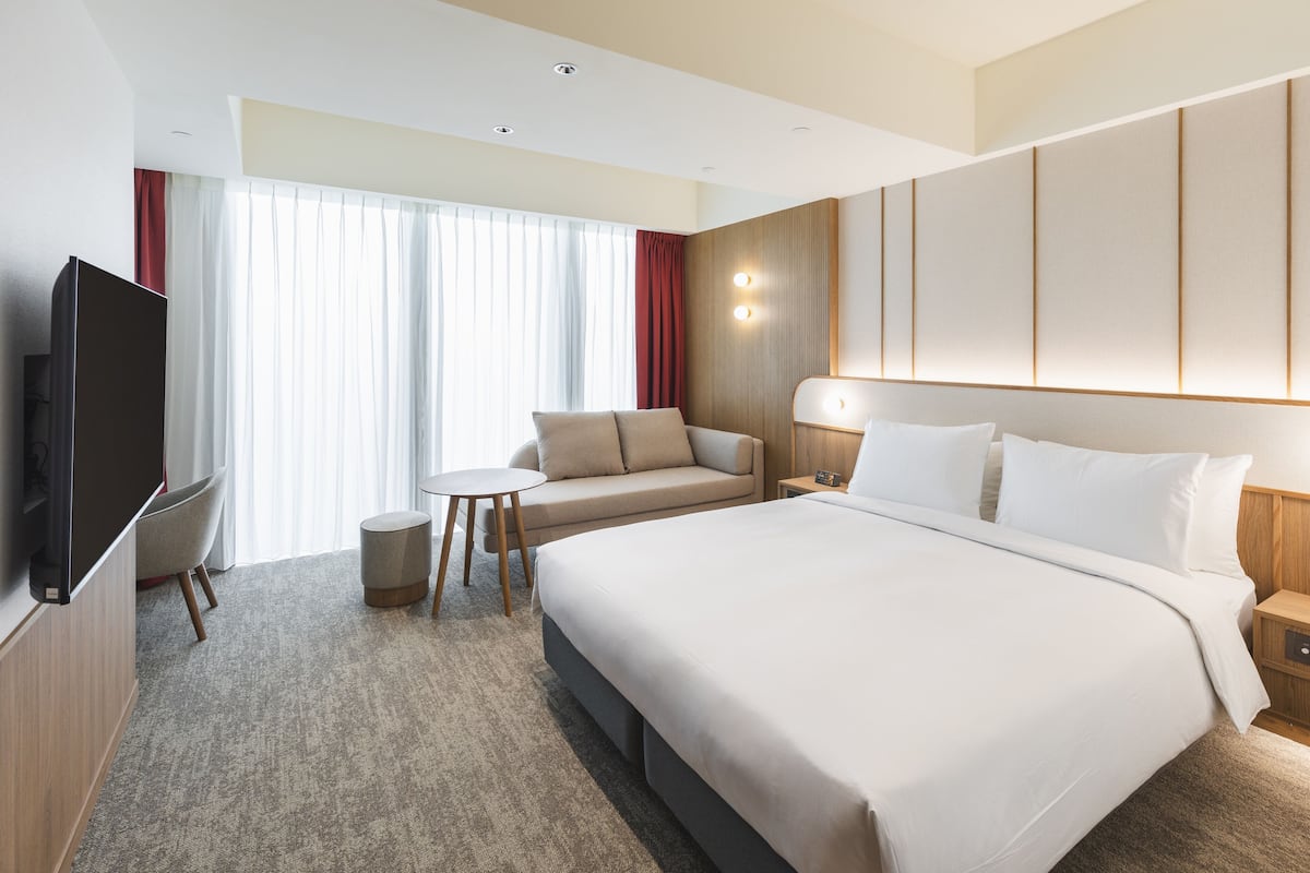 A hotel room with a large bed, a TV, a small table, and a sofa.