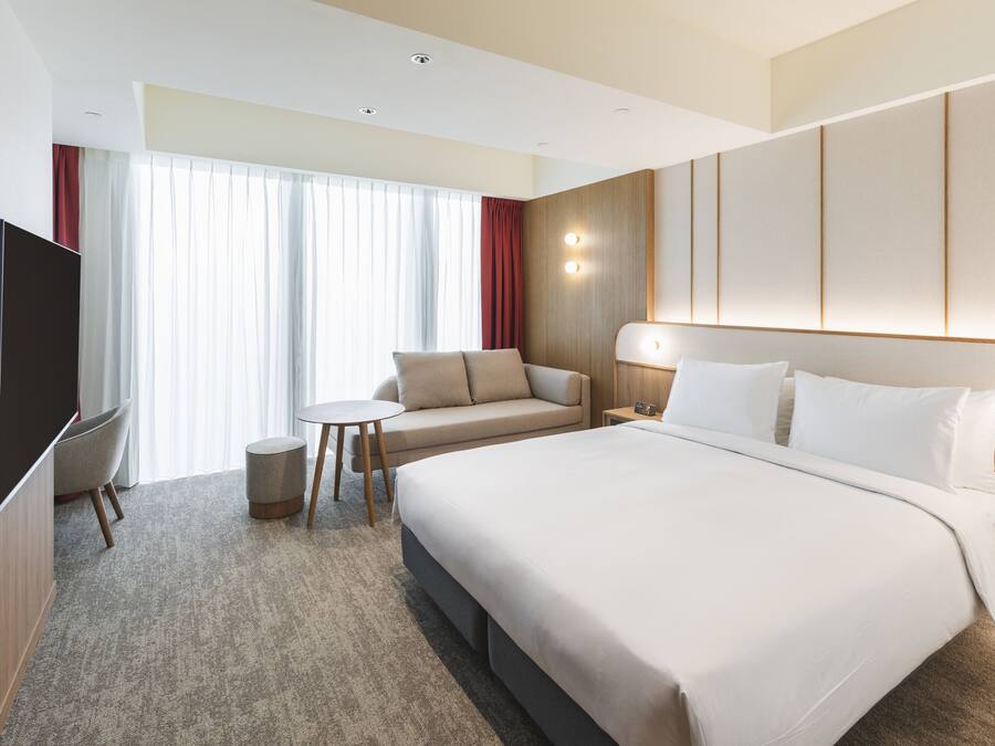 A hotel room with a large bed, a TV, a small table, and a sofa.