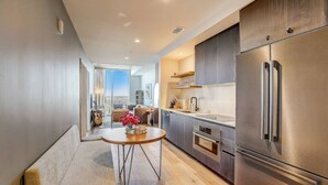 A modern kitchen with a stainless steel refrigerator, wooden cabinets, and a dining area with a round table and bench. - Highrise 1BR Luxe Suite near DT|Vibrant Rainey St (Austin)