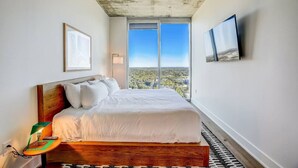A bedroom with a large bed, a view of the city, and a concrete ceiling. - Highrise 1BR Luxe Suite near DT|Vibrant Rainey St (Austin)