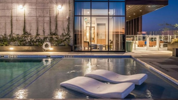A modern hotel with a swimming pool, lounge chairs, and a well-lit interior. - Highrise 1BR Luxe Suite near DT|Vibrant Rainey St (Austin)