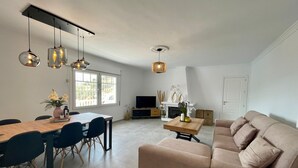 Una sala de estar moderna con un sofá color beige, una mesa de comedor con sillas y un televisor.