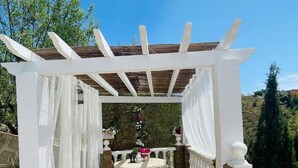 Un patio cubierto con una pérgola, una mesa de piedra y faroles.