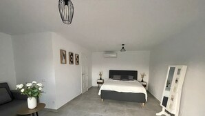 Un dormitorio moderno con una cama grande, una mesita de noche, un espejo y una pequeña zona de estar con una mesa y flores.