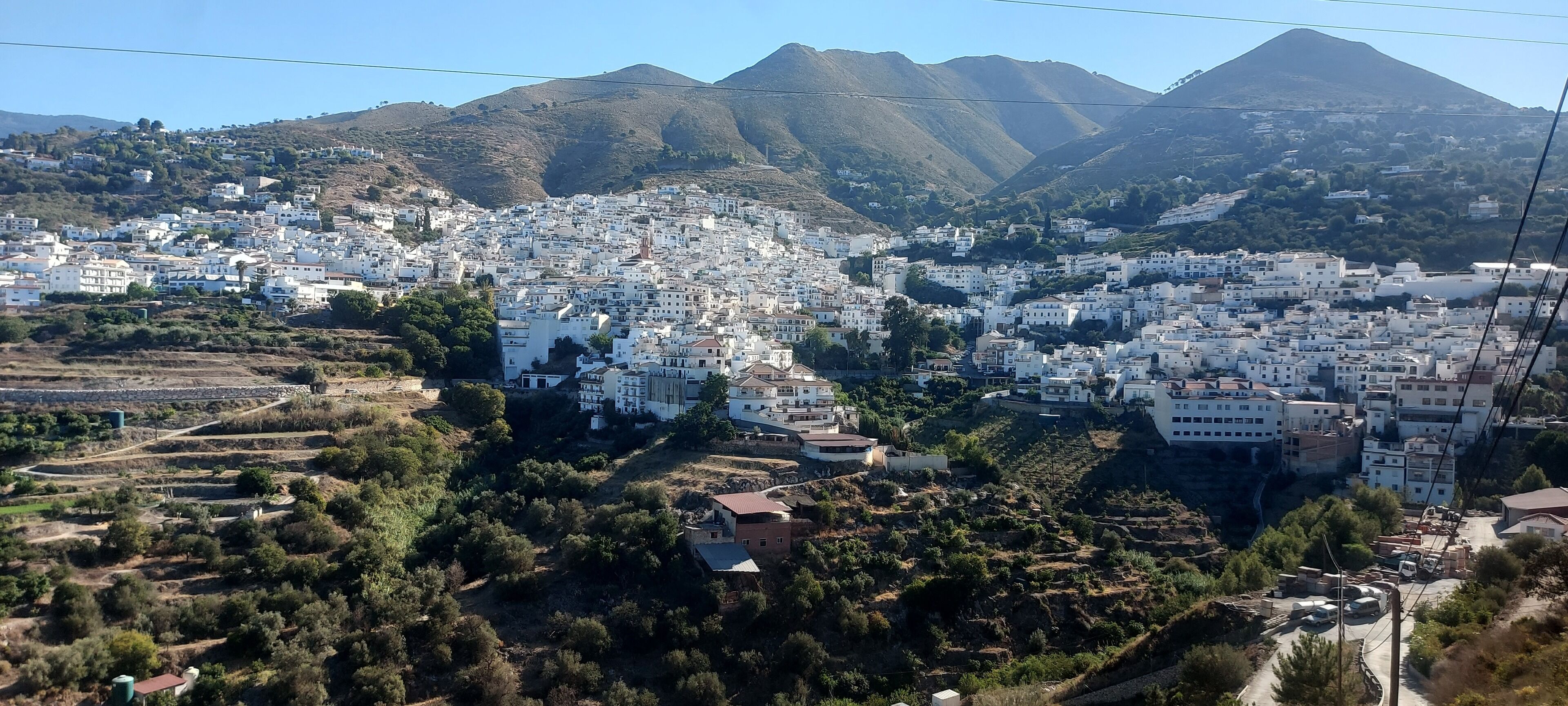 A town with white buildings, a mountainous backdrop, and a mix of residential and agricultural areas.