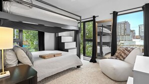 A modern hotel room with a bunk bed, a sofa, a desk, and a large window offering a city view. - Downtown Nashville | Pool, Gym + Skyline Views | Bridgestone (Nashville)