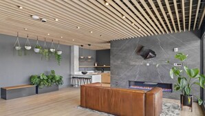 A modern interior with a wooden ceiling, a stone wall with a fireplace, and a seating area with a bench and a coffee table. - Downtown Nashville | Pool, Gym + Skyline Views | Bridgestone (Nashville)