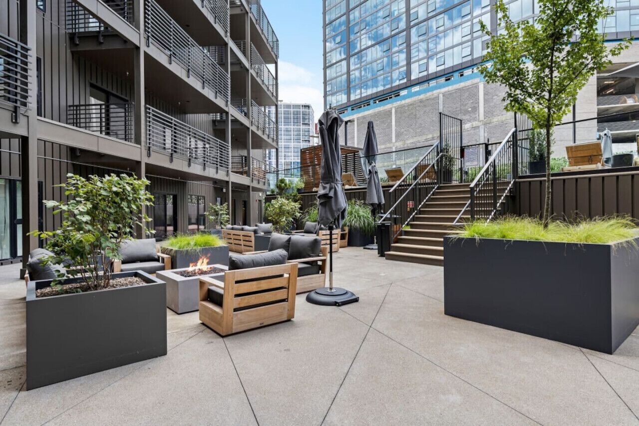 A modern outdoor seating area with sofas, planters, and a fire pit.
