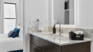 A modern bathroom with a marble sink, a large mirror, and a black basket with towels. - Riverfront Group Suite: Walk to Broadway & Titans Stadium (Nashville)