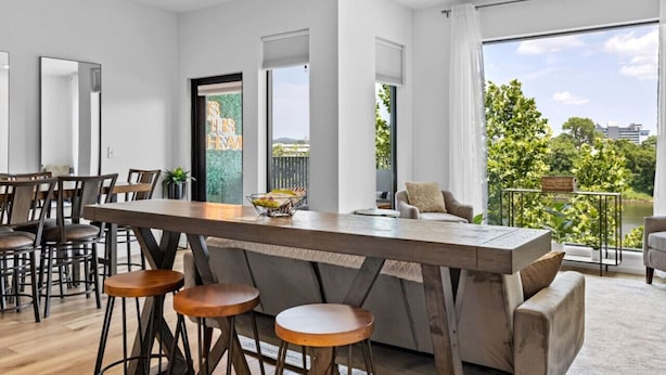 A modern kitchen with a central island, bar stools, and a view of greenery outside. - Riverfront Group Suite: Walk to Broadway & Titans Stadium (Nashville)