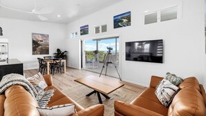 Ett modernt vardagsrum med en soffa, ett soffbord och en matplats med stolar och ett bord. Det finns en balkong med en kamera på ett stativ.