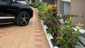 Un bâtiment moderne avec un toit recouvert de tuiles rouges, une allée pavée et une variété de plantes aux couleurs vives le long du chemin.