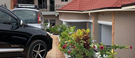 A modern building with a red-tiled roof, a paved driveway, and a variety of colorful plants along the pathway.