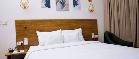 A hotel room with a wooden headboard, white bedding, a green chair, and three wall-mounted artworks.