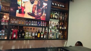 A bar area with shelves of various liquor bottles and a television screen displaying a program. - Velvet Suites (Kigali)