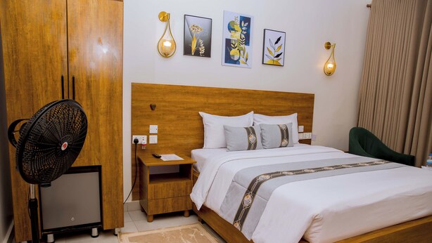 A hotel room with a wooden bed, a nightstand, a desk with a fan, and artwork on the wall. - Velvet Suites (Kigali)