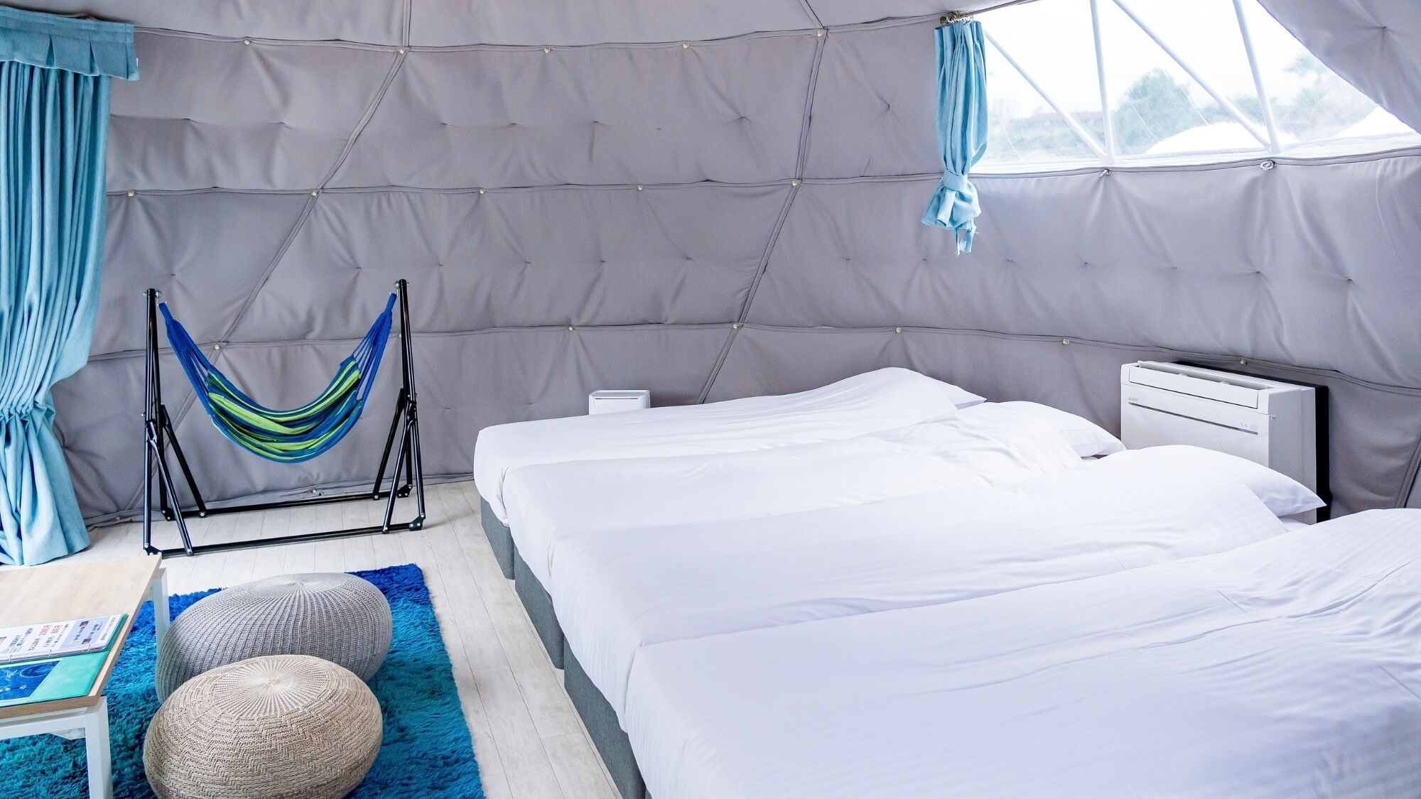 A tent-style room with two beds, a hammock, and a small table with a book.