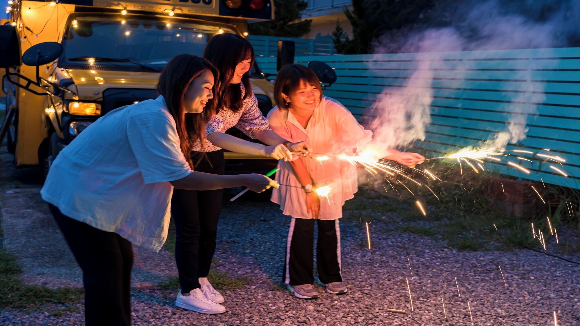 Three people holding sparklers outdoors at dusk.