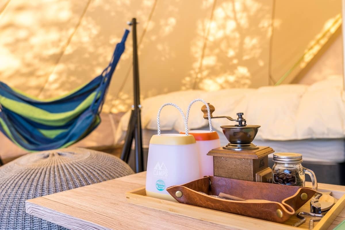 A hammock, a bed with white bedding, a coffee maker, and a tray with a leather case and utensils.