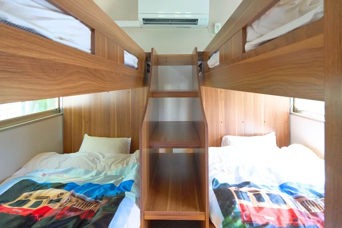 A bunk bed room with a wooden ladder, white bedding, and a window.