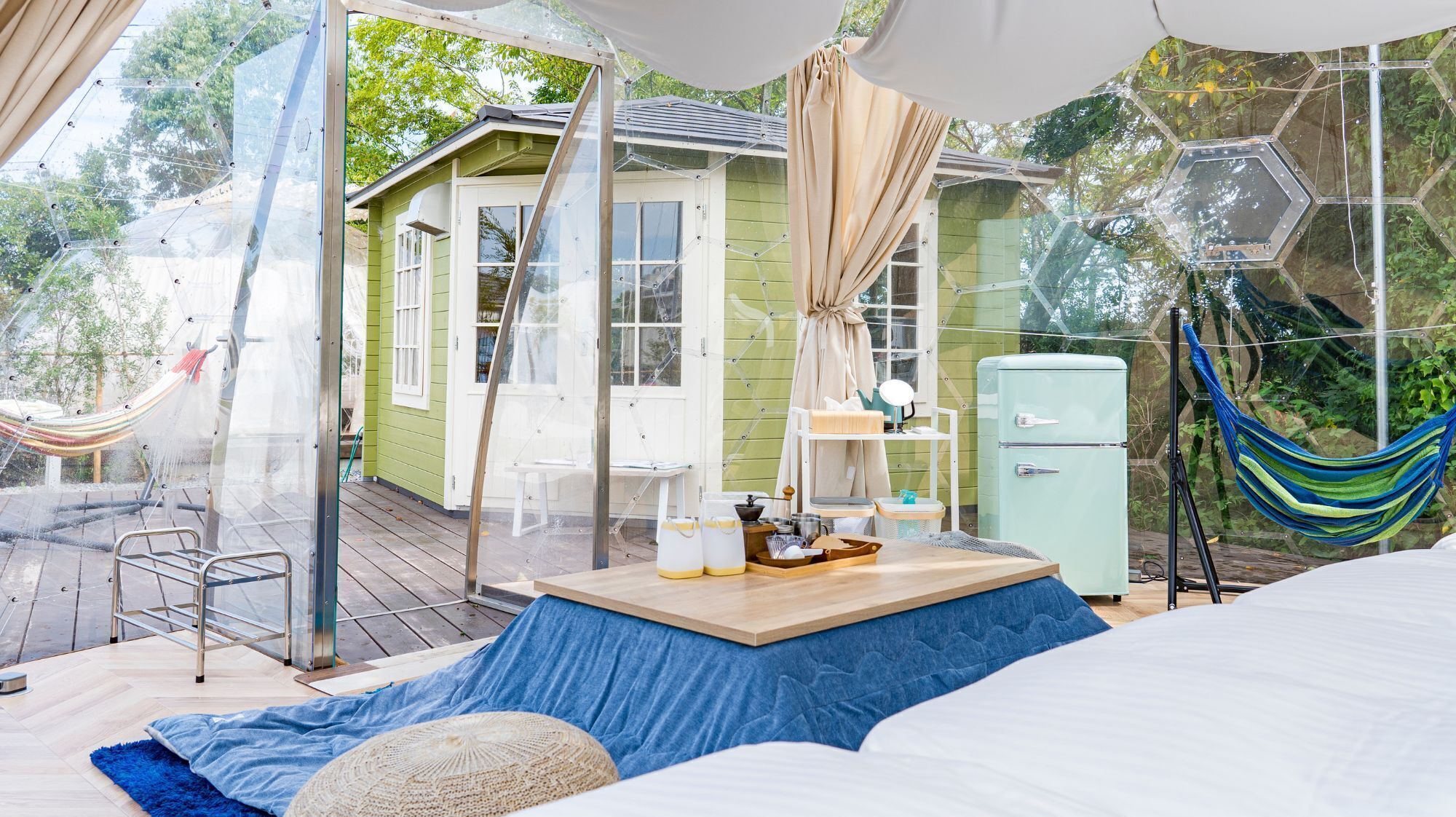 A cozy outdoor living space with a hammock, a small table with items, and a vintage-style refrigerator.
