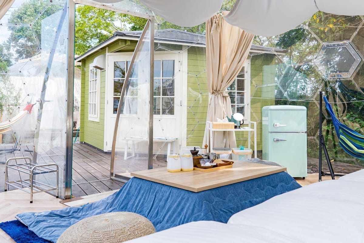 A cozy outdoor living space with a hammock, a small table with items, and a vintage-style refrigerator.