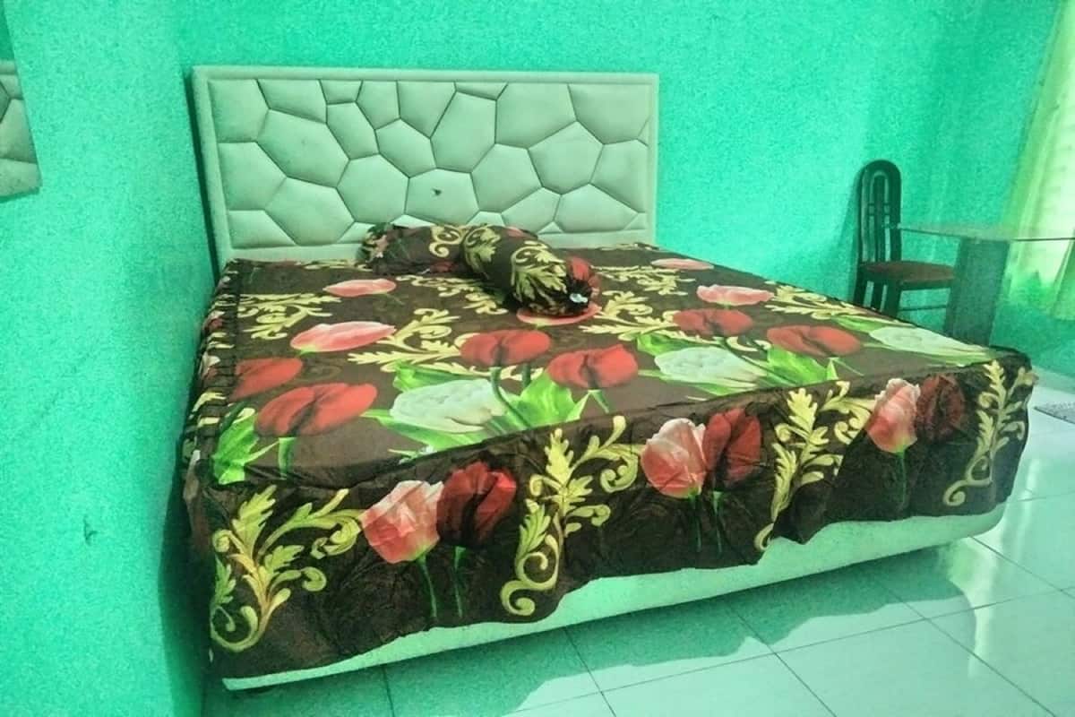 Een bed met een bloemenbedekker en een gestoffeerd hoofdeinde in een kamer met groene wanden.