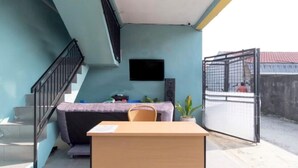 Ein Zimmer mit Schreibtisch, Stuhl und einer kleinen Couch. Eine Treppe befindet sich links und ein Tor rechts.