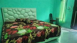 Ein Bett mit floralem Überwurf, einem gepolsterten Kopfteil und einem Sessel neben einem Fenster mit Vorhang.