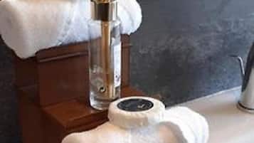 A bathroom with a wooden towel rack holding two white towels, a glass bottle with a pump, and several small bottles with labels.