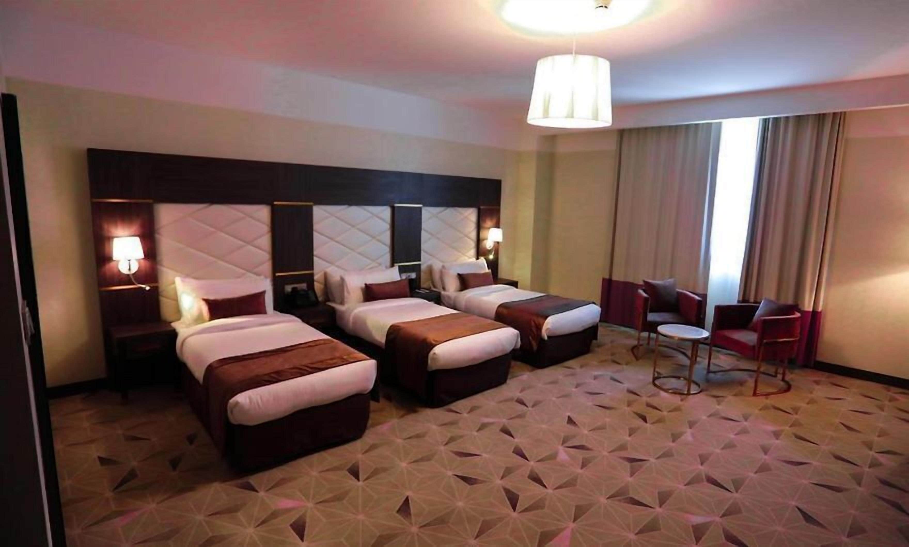 A hotel room with three beds, a small seating area, and a large window with curtains.