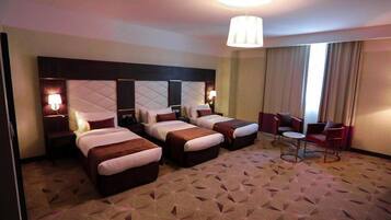 A hotel room with three beds, a small seating area, and a large window with curtains.