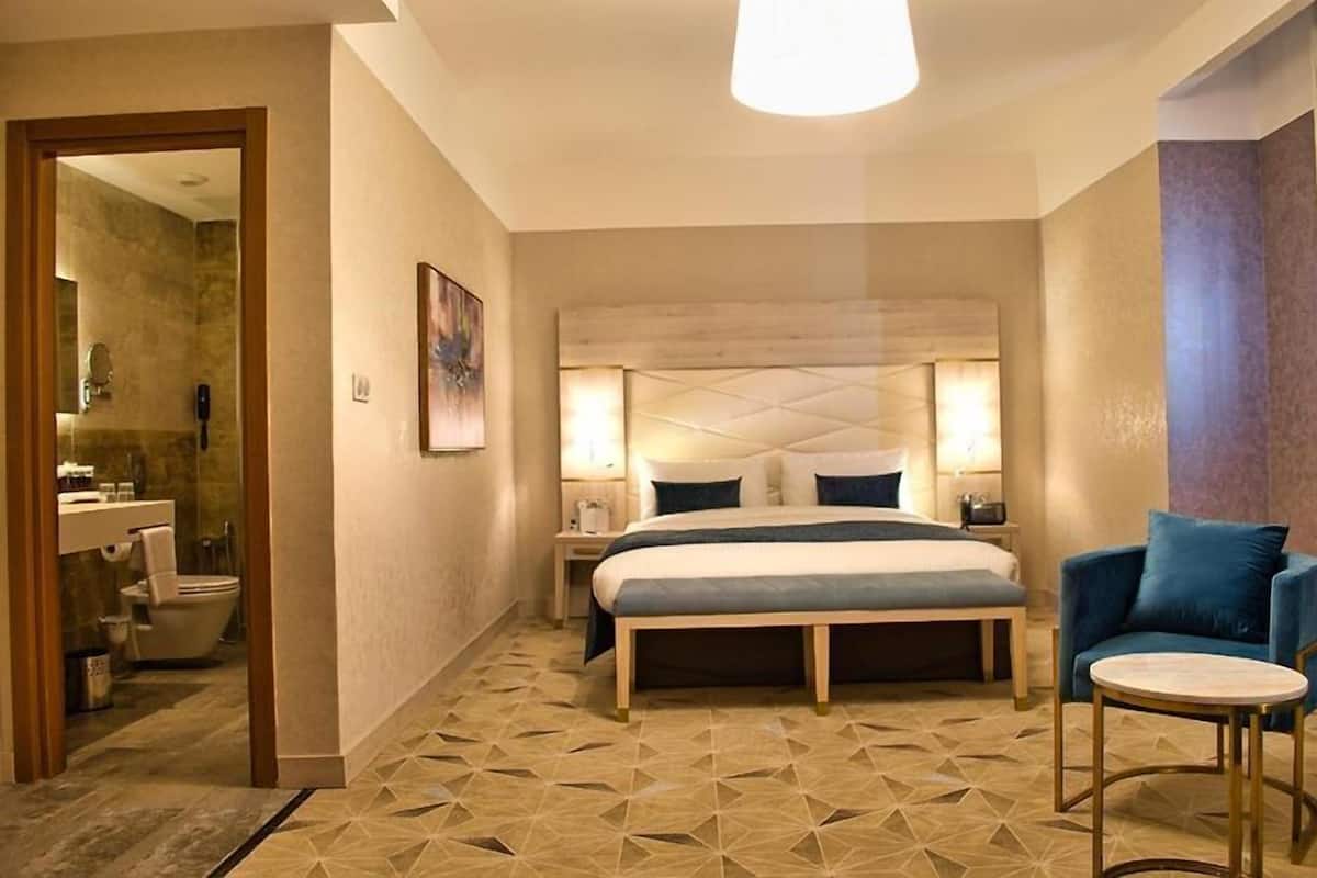 Una habitación de hotel con una cama grande, mesitas de noche, una silla y una pequeña mesa.