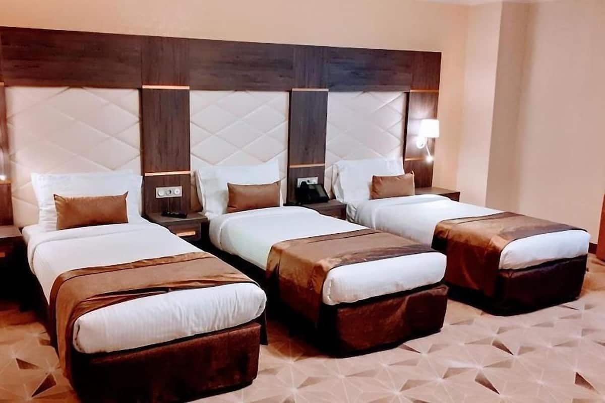 Habitación de hotel con tres camas, cada una con cabecero de madera y una mesita de noche.
